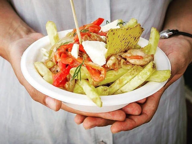 Une personne tient entre ses mains un bol de poutine garnie de poulet, poivrons et tomates. Une personne tient entre ses mains un bol de poutine garnie de poulet, poivrons et tomates.