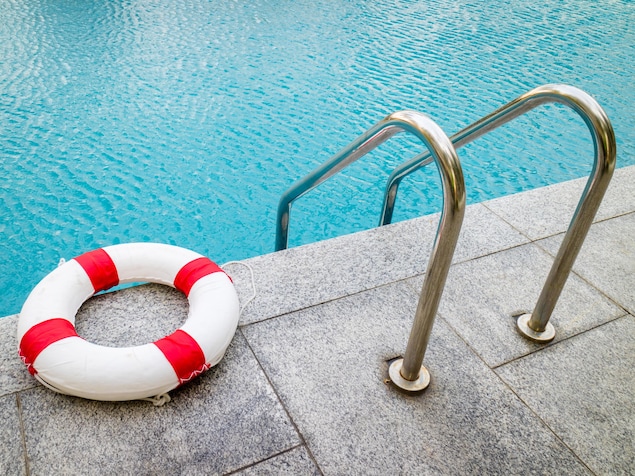 Une bouée de sauvetage rouge et blanche déposée en bordure d'une piscine creusée.