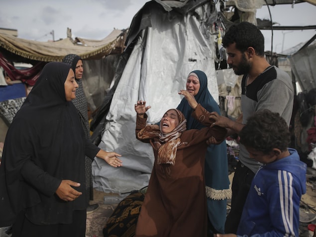 Une femme en pleurs au milieu d'autres personnes et d'un camp en ruines.