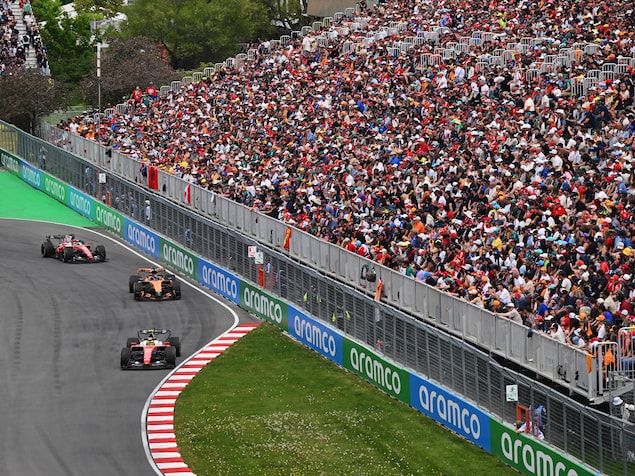 Une foule observe trois voitures de course.