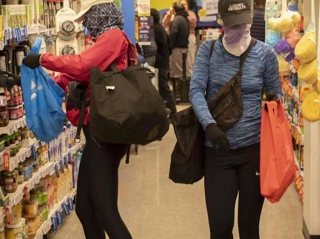Des personnes dont le visage est caché mettent des items dans des sacs dans une allée d'épicerie.
