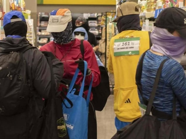 Des personnes dont le visage est caché mettent des items dans des sacs dans une allée d'épicerie.