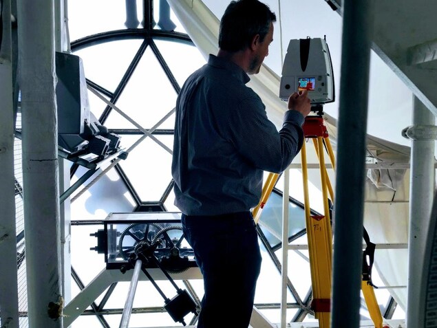 On voit un homme, de dos, qui manipule un appareil servant à scanner les éléments d'architecture. Devant lui se trouve les mécanismes de l'horloge du parlement. On voit un homme, de dos, qui manipule un appareil servant à scanner les éléments d'architecture. Devant lui se trouve les mécanismes de l'horloge du parlement.