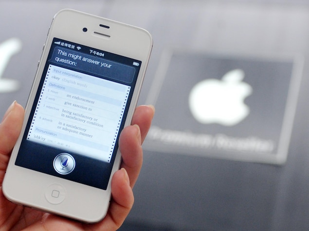 Une main tient un iPhone, qui affiche l'interface de l'assistant vocal Siri.