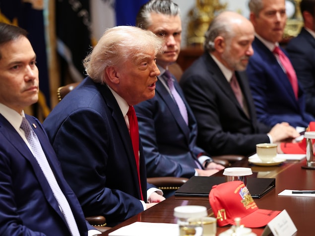 Donald Trump parle aux membres de son Cabinet devant une table où sont déposées des tasses et des casquettes rouges.