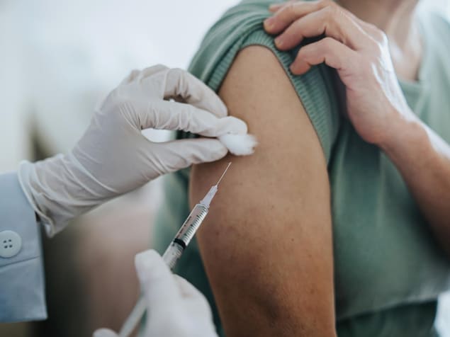 Gros plan sur une femme âgée recevant le vaccin contre la COVID-19 dans le bras, administré par un médecin à l'hôpital.