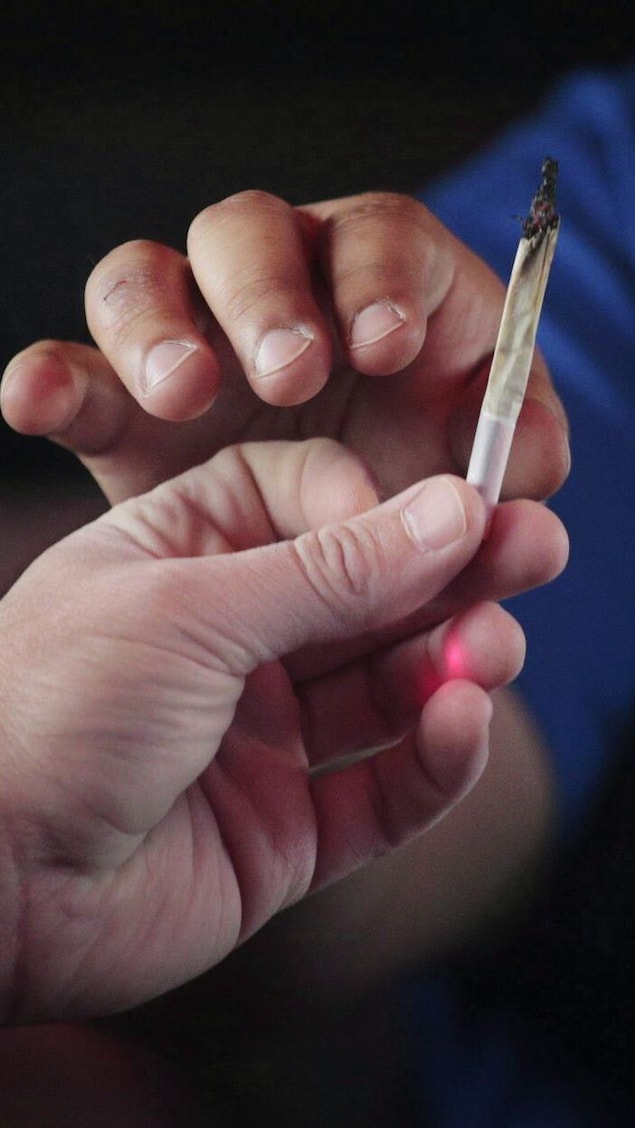 Un joint de cannabis est échangé entre deux personnes, dont on ne voit pas les visages.