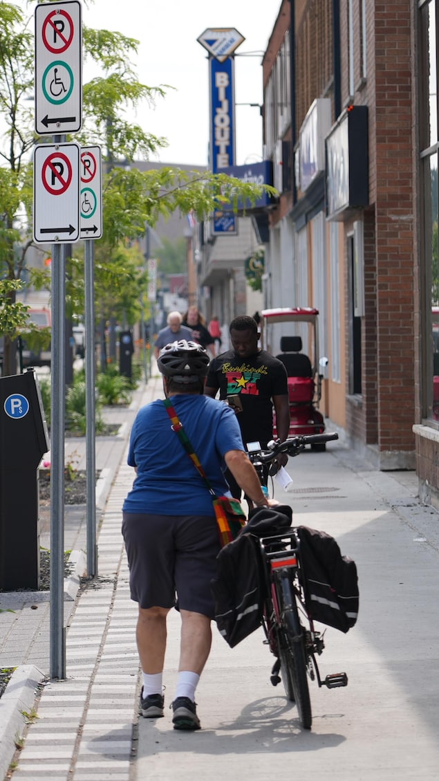 Une dame, de dos, marche à côté de son vélo sur un trottoir, au centre-ville de Val-d'Or.