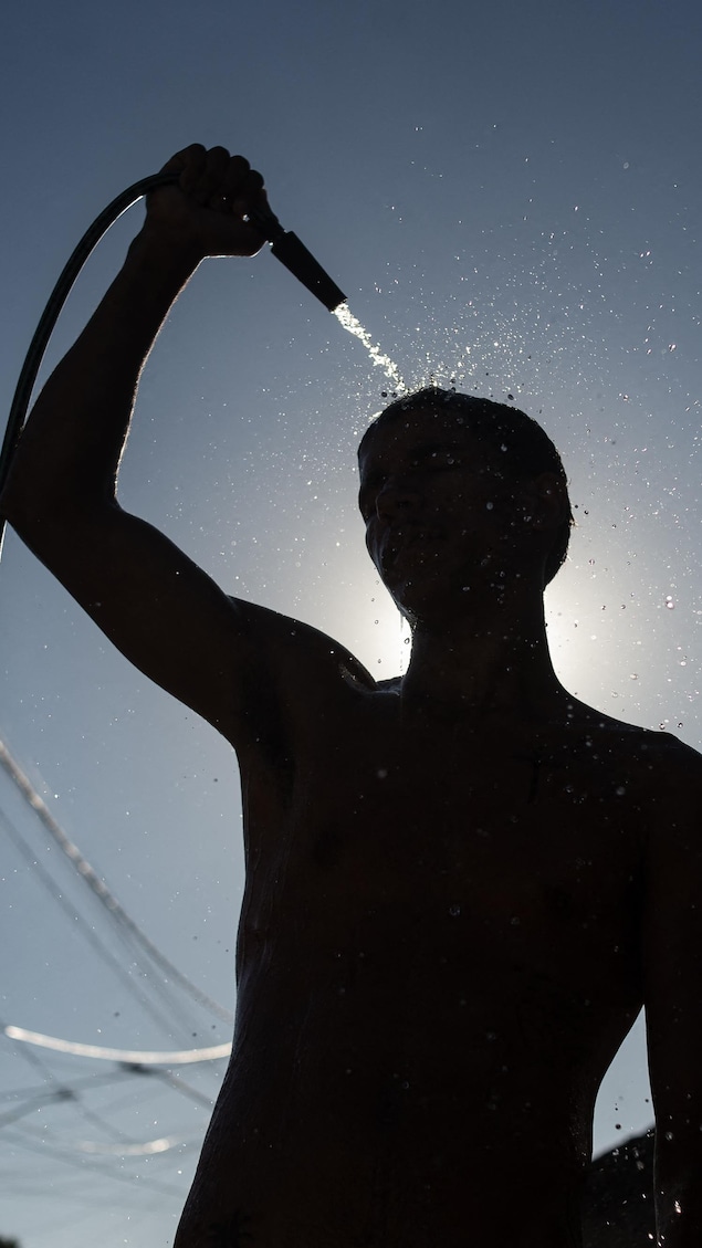 Un homme se rafraîchit à l'aide d'un tuyau d'arrosage.