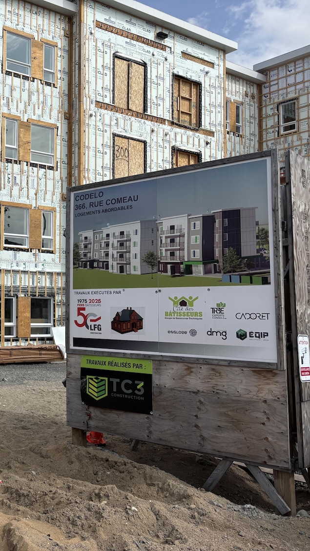 Un immeuble en construction recouvert de panneaux isolants se dresse devant un panneau d'affichage du projet.