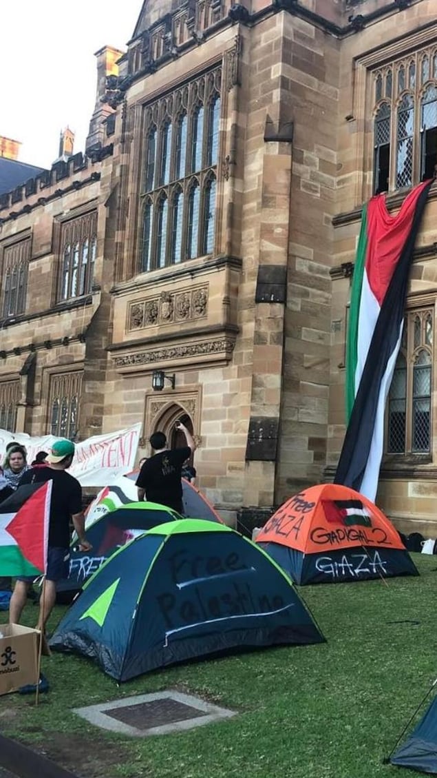 Des étudiants se tiennent aux côtés de tentes et de drapeaux palestiniens devant l'université.