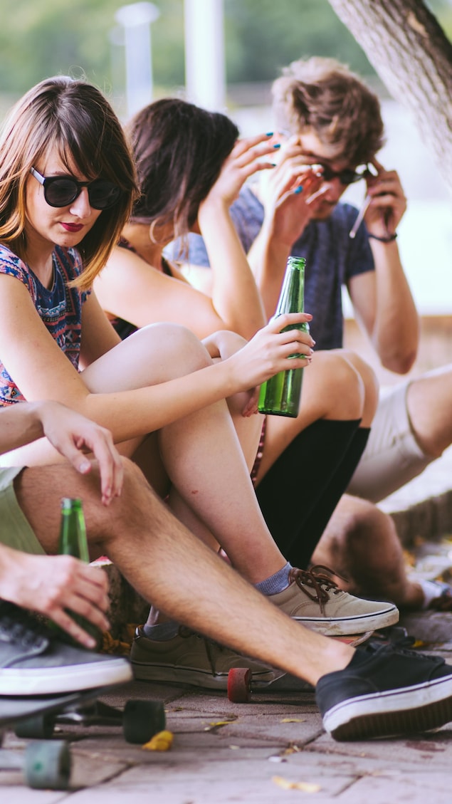 Quatres jeunes qui semblent d'âge mineur sont assis sur une chaîne de trottoir avec des skateboards et des bouteilles de bière.