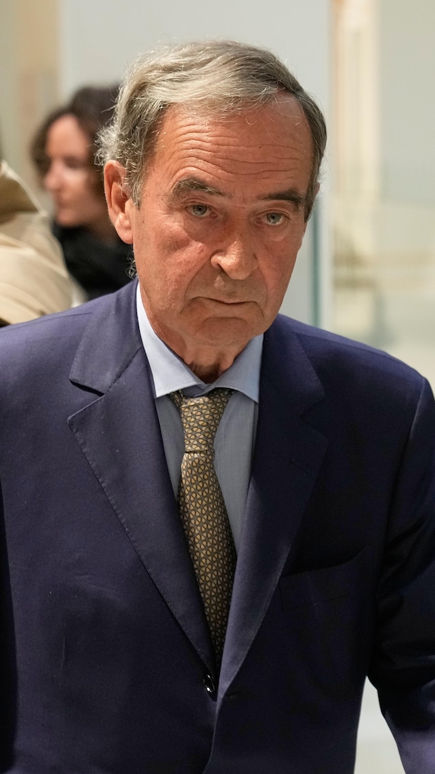 Un homme marche près de policiers, talonné par son avocat.