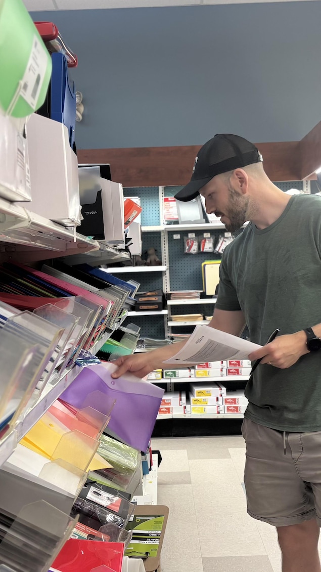 Maxime Clément sélectionne des fournitures scolaires dans une rangée de la Biblairie GGC.