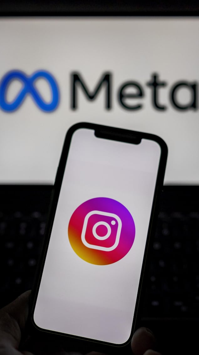 Un téléphone affichant le logo d'Instagram est brandi devant le logo de Meta.