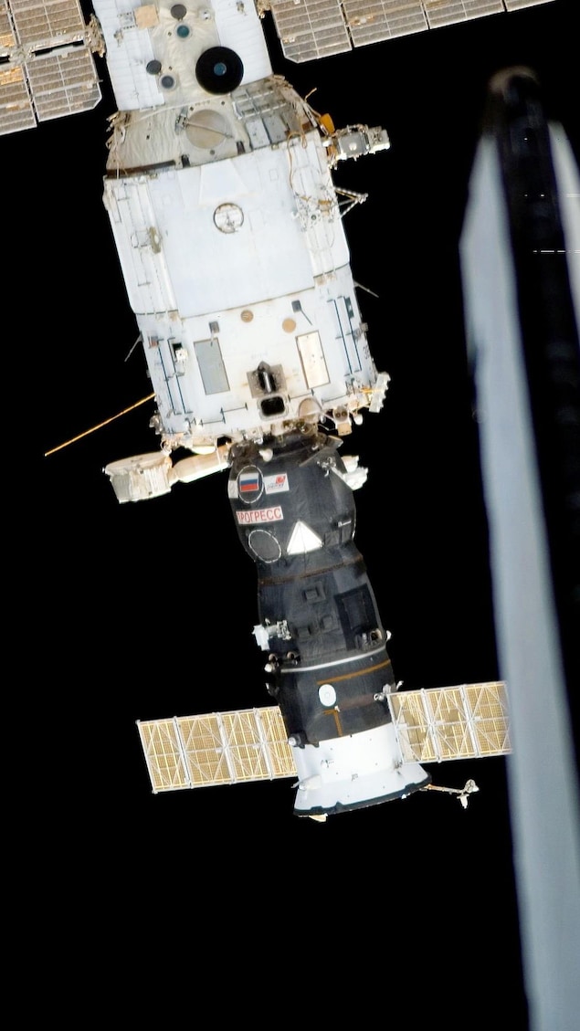 Un vaisseau est amarré à un bout cylindrique de la station spatiale internationale.