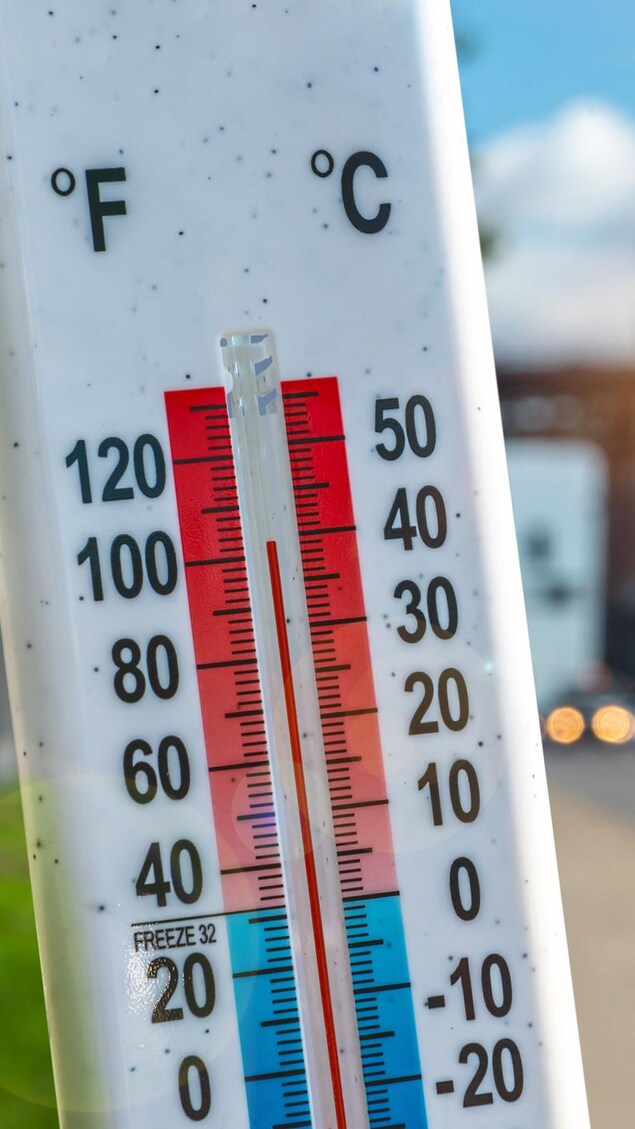 Un thermomètre devant les voitures et la circulation pendant la canicule à Montréal.