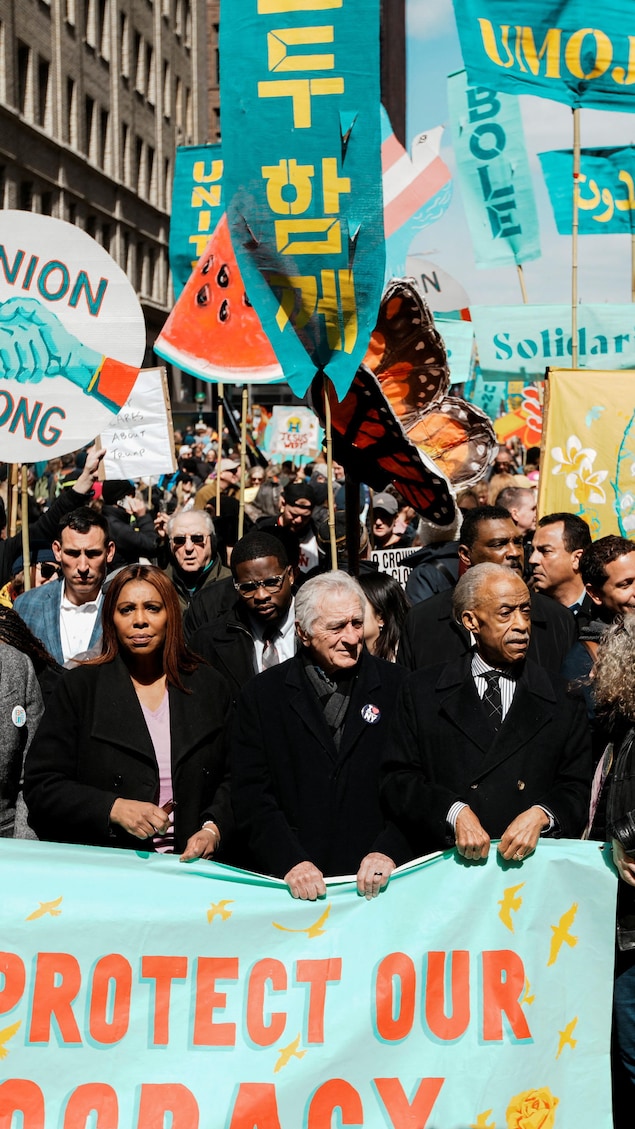 Une foule de manifestants marche dans les rues de New York en portant des pancartes et une grande bannière.
