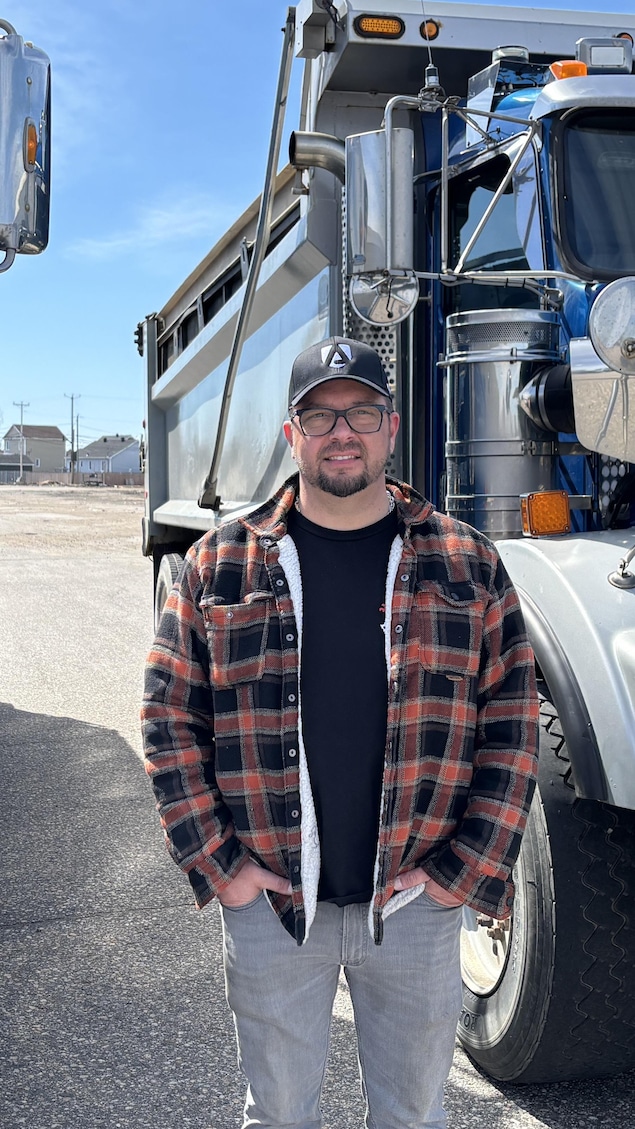 Patrick Lelièvre se tient debout entre deux gros camions. 
