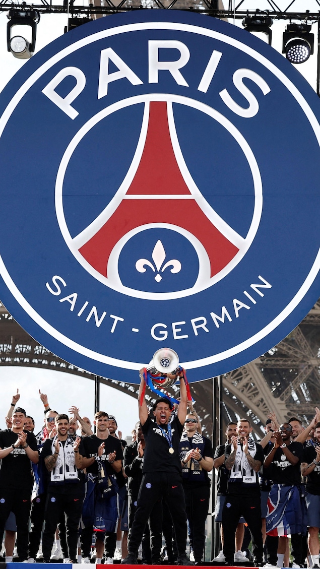 Des athlètes du club de soccer Paris Saint-Germain célèbrent leur victoire à la Ligue des champions en brandissant un trophée au pied de la tour Eiffel, à Paris.
