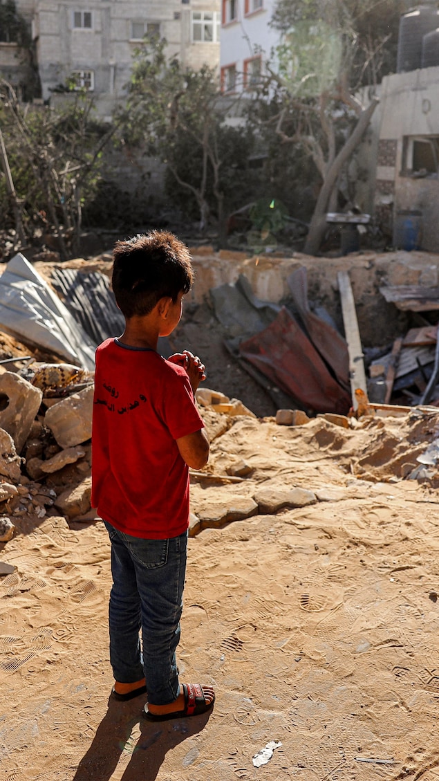 Un enfant se tient devant les débris d'un bâtiment.