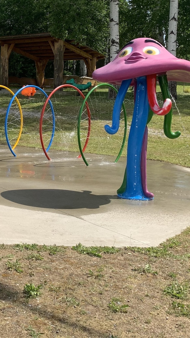 Des jeux d'eau dans un parc de Rivière-Héva, avec une glissoire et un boisé en arrière-plan.