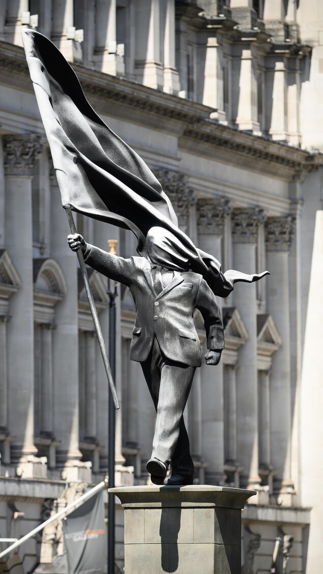 Statue à Londres représentant un homme s'éloignant d'un socle en tenant un drapeau au vent qui lui couvre le visage. 