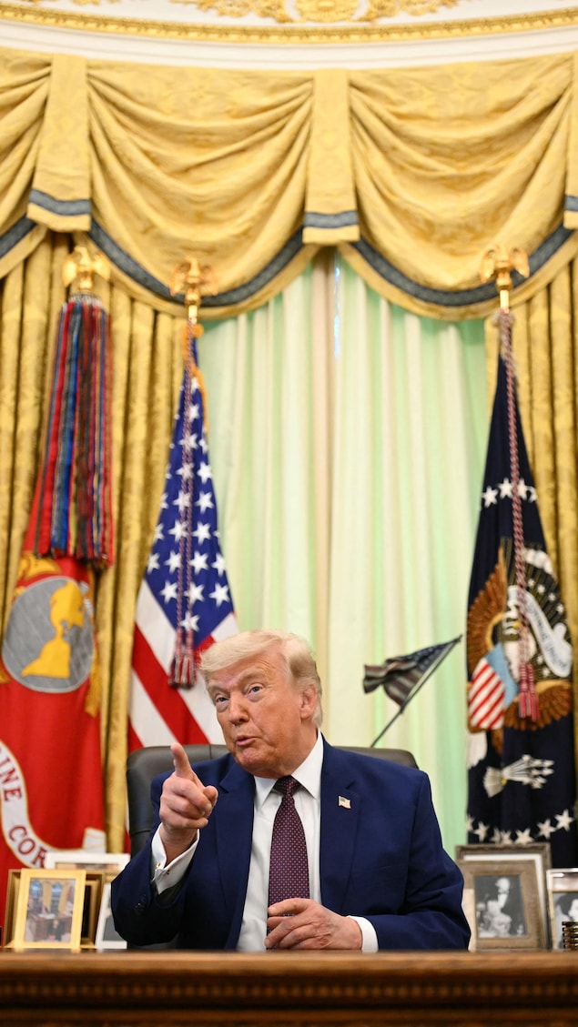 Donald Trump assis dans le bureau ovale, devant des drapeaux et des rideaux dor&eacute;s.