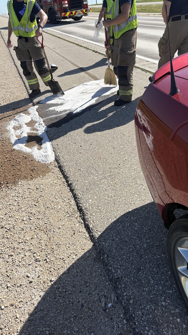 Trois pompiers s'affairent à remédier à une fuite d'essence provenant d'une auto sur une autoroute.