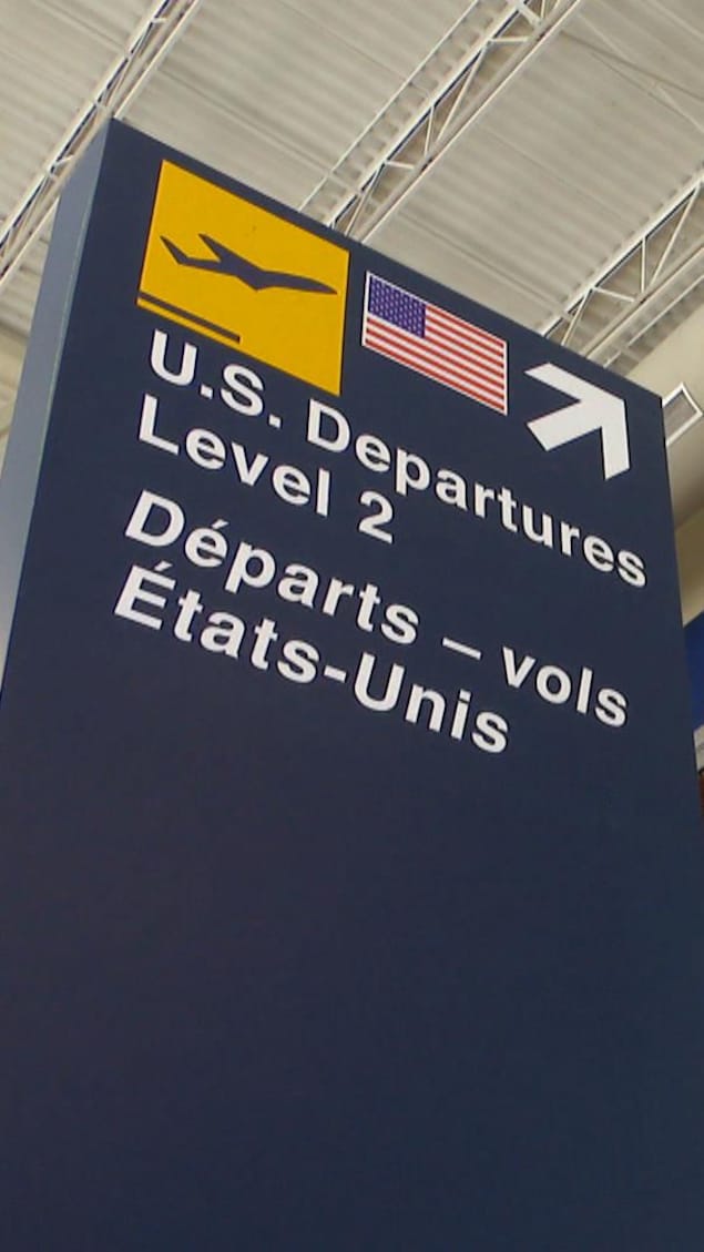 L'enseigne dans l'aéroport qui pointe vers un escalier roulant pour se rendre à l'endroit pour les départs des vols vers les États-Unis.