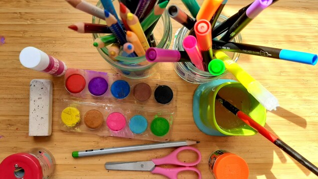 Des gobelets de crayons posés sur une table avec de la peinture.