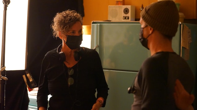 Femme debout avec un masque qui regarde un homme de dos.