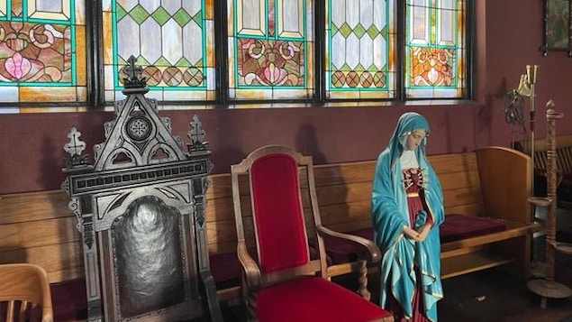 Deux chaises et une statue de vierge devant des vitraux dans une église.