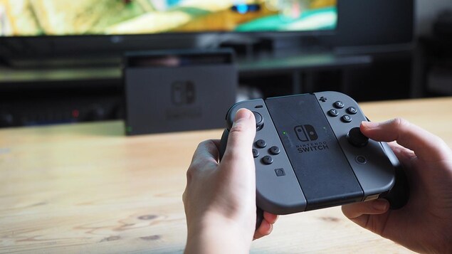 Une personne tient dans ses mains les manettes d'une console de jeux Nintendo Switch.