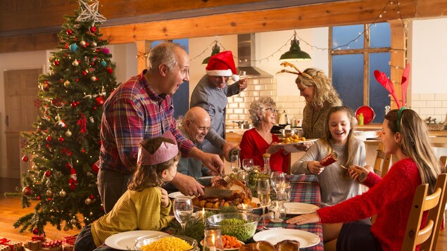 Une famille est assise autour d'une table. Il y a un sapin de Noël. 