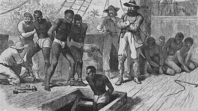 illustration : des hommes sont enchainés et mis en cale d’un navire
une légende en anglais est écrite dessous : « on board a slave-ship »