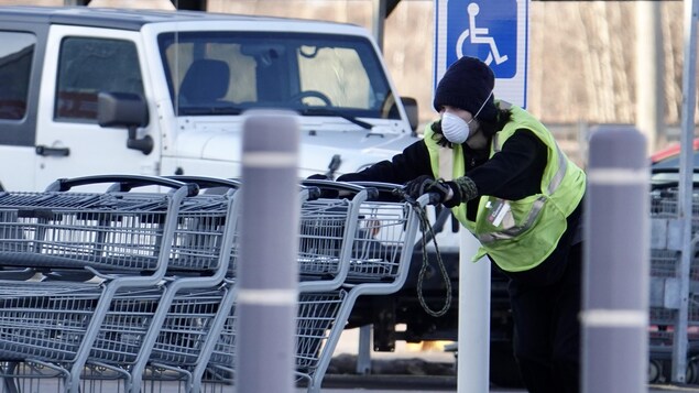 Un travailleur portant un masque pousse des paniers d'épicerie.