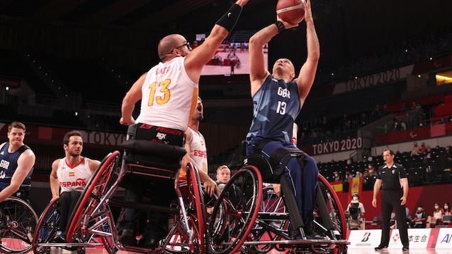 Un joueur de basketball en fauteuil roulant Britannique tente un tire contre un joueur Espagnol.