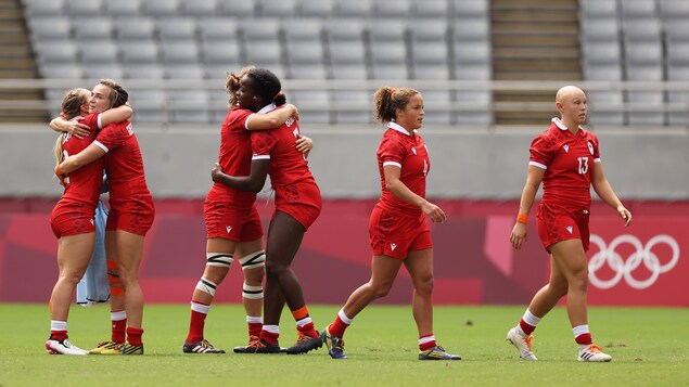 Des joueuses de l'équipe canadienne se félicitent après la victoire sur le Kenya. Sur le terrain, quatre joueuses s'enlacent en groupes de deux. Deux autres joueuses marchent vers la droite de la photo.