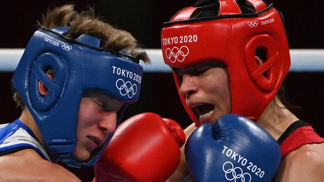 Deux boxeuses sont au corps à corps alors que l'athlète en rouge vient de frapper durement son adversaire en bleu d'un coup droit.