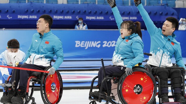 Trois paracurleurs chinois célèbrent leur victoire en criant et en levant les bras dans les airs. // Beijing 2022 Winter Paralympic Games - Wheelchair Curling - Gold Medal Match - China v Sweden - National Aquatics Center, Beijing, China - March 12, 2022. Chen Jianxin of China, Zhang Mingliang of China and Yan Zhuo of China react. REUTERS/Peter Cziborra