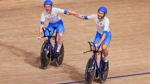 Simone Consonni et Filippo Ganna de l'équipe d'Italie sont sur leur vélo se tenant le bras après avoir remporté la médaille d'or lors de la finale de poursuite par équipes.