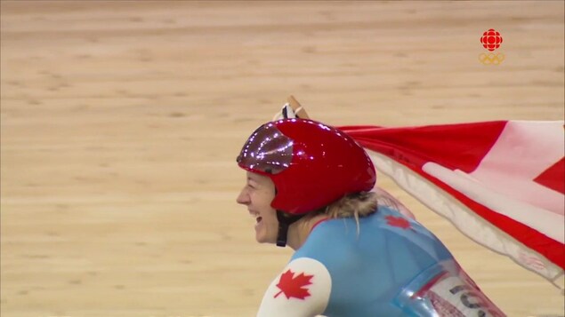 La cycliste canadienne Kelsey Mitchell soulève le drapeau canadien après avoir remporté la finale du sprint en cyclisme sur piste.