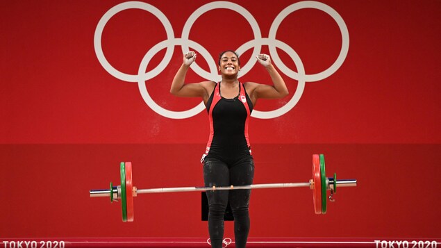 Une jeune femme a les bras dans les airs pour célébrer après avoir levé une charge importante en haltérophilie aux Jeux olympiques.