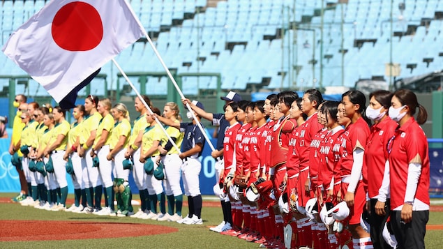 Les joueuses des deux équipes, en rouge et en jaune, regardent dans la même direction pendant la présentation des cérémonie officielles avant un match de softball.