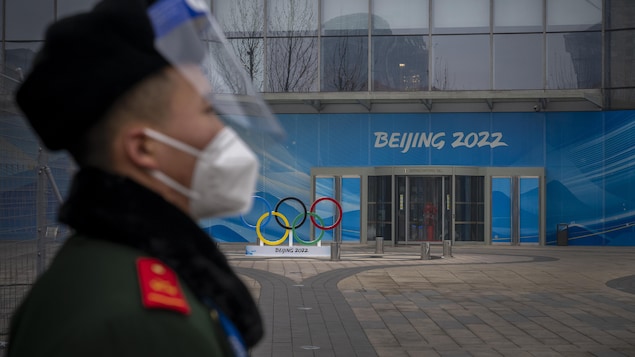 Un garde de sécurité avec un masque et une visière se tient devant un bâtiment olympique à Pékin.