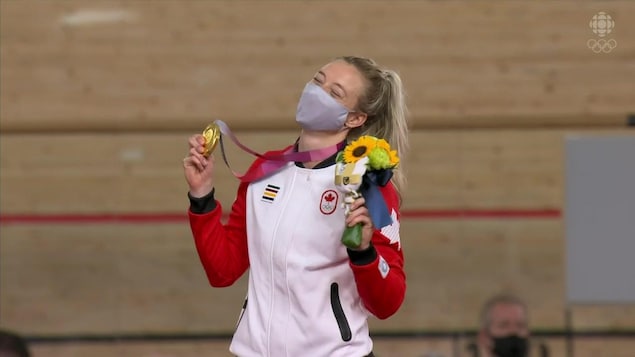 Une femme tient une médaille d'or et un bouquet de fleur dans l'autre main.