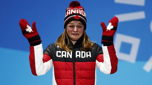 Une athlète canadienne sanglote sur le podium olympique à Pyeongchang. Elle lève partiellement ses bras et présente ses mains.
