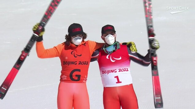 Deux skieurs se font l'accolade en levant chacun un ski en posant pour la caméra.