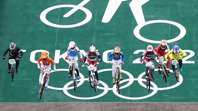 Huit cyclistes dont Drew Mechielsen sont en piste sur leur BMX et sont alignées les unes à côté des autres. Elles s'apprêtent à effectuer un saut lors de la demi-finale.